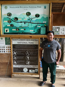 A Park Ranger, in front of a wooden kiosk with a trail map, Mayflower Bocawina National Park, Belize.