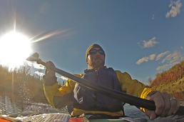 A kayaker, shown from the front, wearing a life vest and paddling a river.