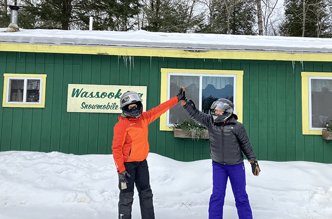 Two Maine Bureau of Parks and Lands staff wearing snowmobile helmets and gear at a break in Dexter, Maine.