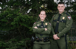 male and female game warden in uniform with pine tree background