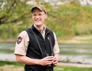 Wildlife biologist smiling with binoculars around neck wearing tan shirt with MDIFW shield on shoulder