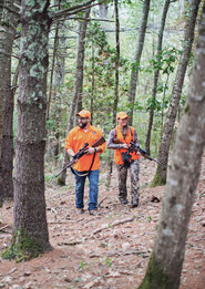 two deer hunters walking through oak trees with orange and camo clothing