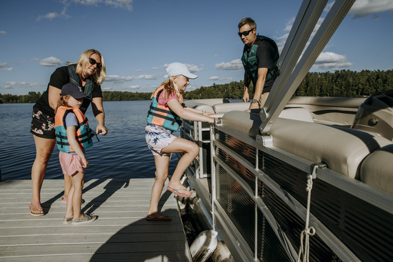 family getting on a pontoon boat wearing brightly colored life jackets