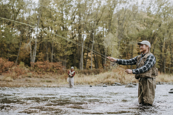 two fly anglers in a river wearing warm clothes with subtle fall foliage colors in background