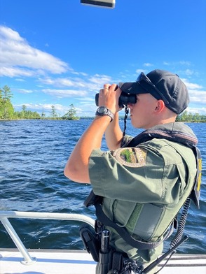 Deputy Game Warden looking through binoculars on bright sunny day on a boat