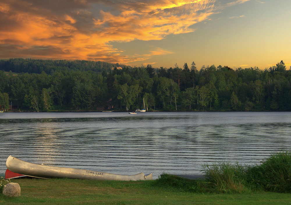 Rangeley lake with sunset, canoe on shore and a motorboat in background