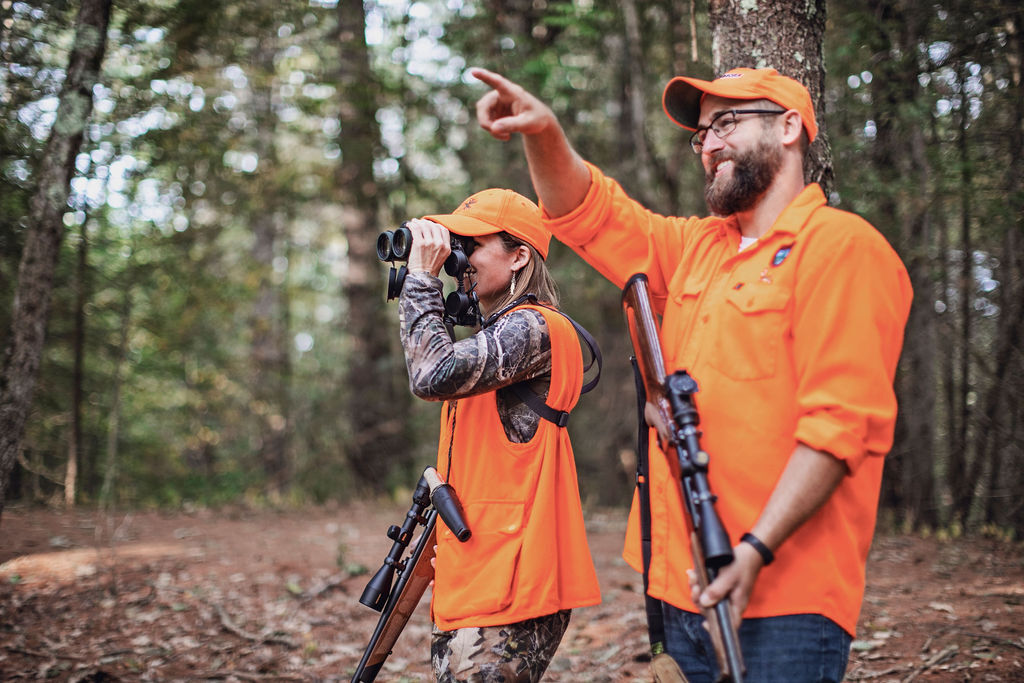 deer hunters glassing a field and another hunter pointing both wearing hunter orange and camo