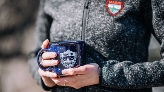 person holding a blue coffee mug with MDIFW logo wearing a black fleece