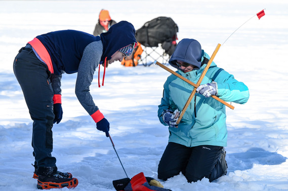 Two people working together to set up an ice fishing trap.