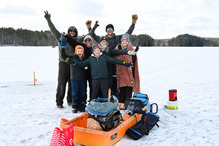 An excited group of people posing for a group photo while ice fishing.