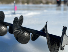 An ice auger lying on a frozen lake with people ice fishing in the background