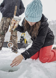 child with blue hat setting an ice fishing trap on a snowy overcast day