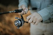 A closeup someone's hands using the reel on a fishing pole