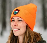A smiling person wearing a blaze orange winter hat with the MDIFW logo on the front