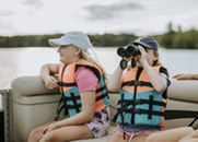 two young girls sitting on a pontoon boat with brightly colored life jackets on