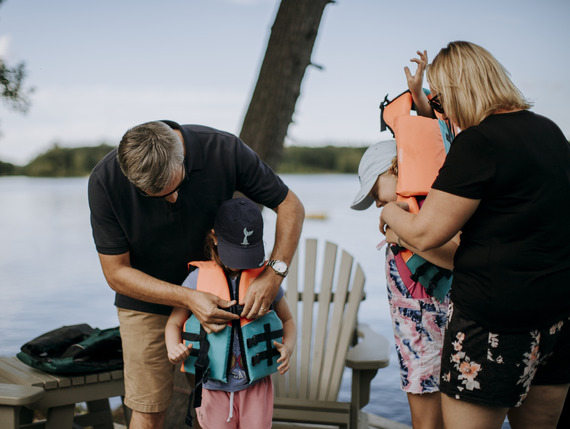 family putting life jackets on dock before a day of boating with bright blue skies