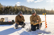 two adult males ice fishing together on blue sunny day