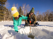 woman and child setting ice fishing trap on bright blue sunny day