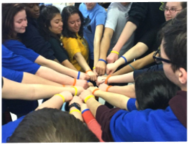 Students’ fist-bumping in a circle with colorful bracelets.