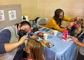 This is a picture of Two adults face painting two children