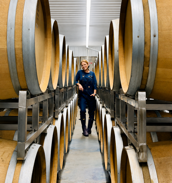 Photograph of Jessica Youngblood standing between two rows of wooden barrels at her metro Detroit vineyard