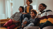 Family of four sitting on a couch laughing and watching tv