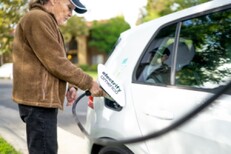 Woman charging an electric vehicle with a fast-charger part of Electrify America's network.