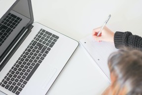 Aerial view of woman writing on notepaper while looking at a laptop