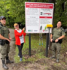 Black Lake Preservation Society member and  DNR Conservation Officers next to Boat Wash sign