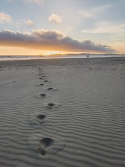 Footprints in the sand with people in the distance walking along the shoreline.