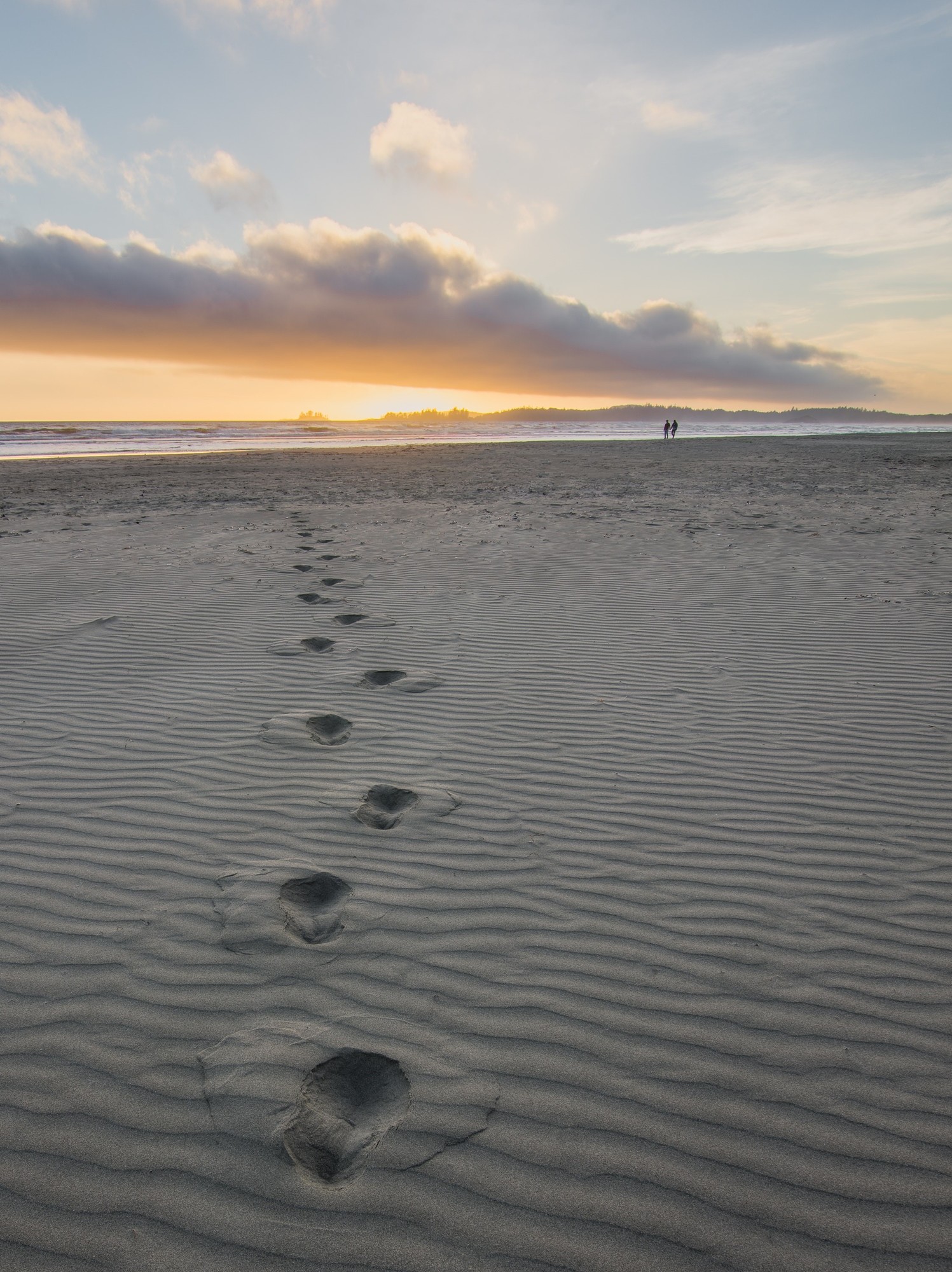 Footprints in the sand with people in the distance walking along the shoreline.