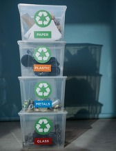 Four recycling tote bins stacked on each other for glass, metals, plastic and paper.