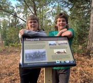 Ben Degeler, left, and Keagan Davis, of Whitefish Township Community School, stand behind the "Logging-The Original Renewable Resource" sign.