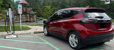 Red SUV using an electric vehicle charger at park.