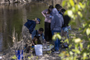 A picture of people studying something on the edge of a body of water.