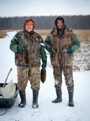 older and younger trappers holding muskrat