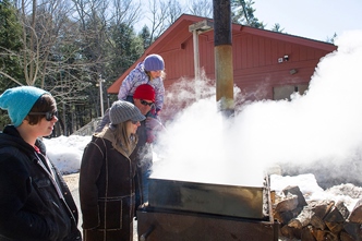 people watching a pan of boiling sap