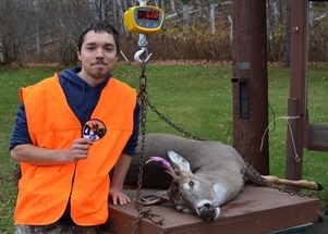 Young man wearing hunter orange, posing with deer on a scale