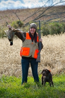 female hunter, holding harvested pheasant, with dog