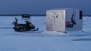 Ice shanty on a frozen lake with a snowmobile next to it