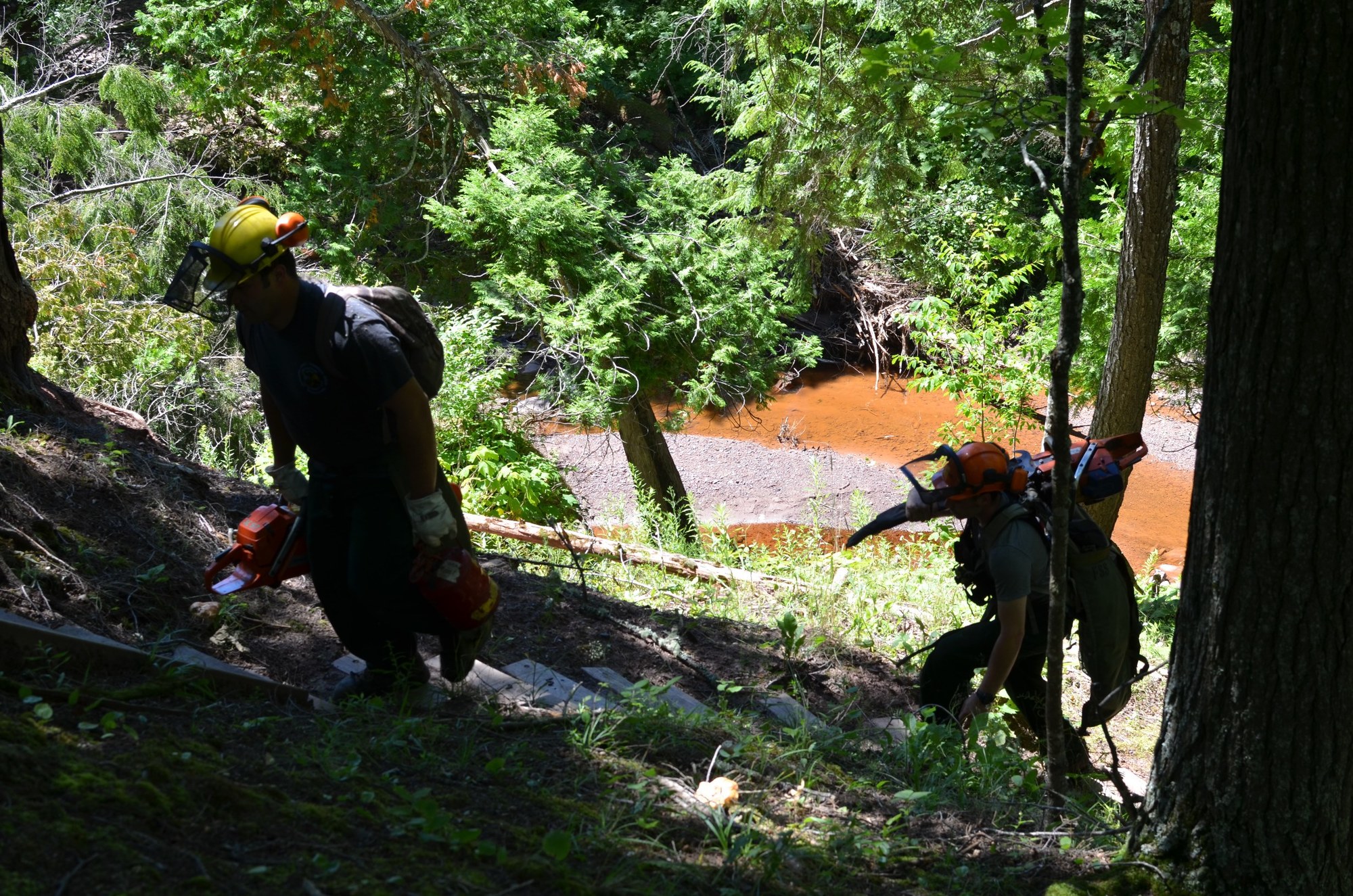 Members of a Michigan Department of Natural Resources crew ascends a flight of stairs, with chainsaws in hand, at Porcupine Mountains Wilderness State