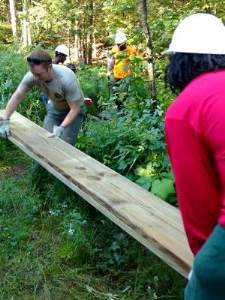 teen volunteer and DNR staffer carry board through forest for boardwalk bridge