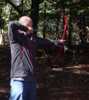 man shooting bow and arrow in wooded setting