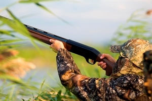 young man in camo aiming shotgun while waterfowl hunting