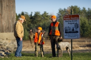 father and daughter pheasant hunters talk to landowner near HAP sign, with dog