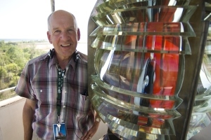 Tawas Point Lighthouse volunteer keeper stands next to lighthouse lens