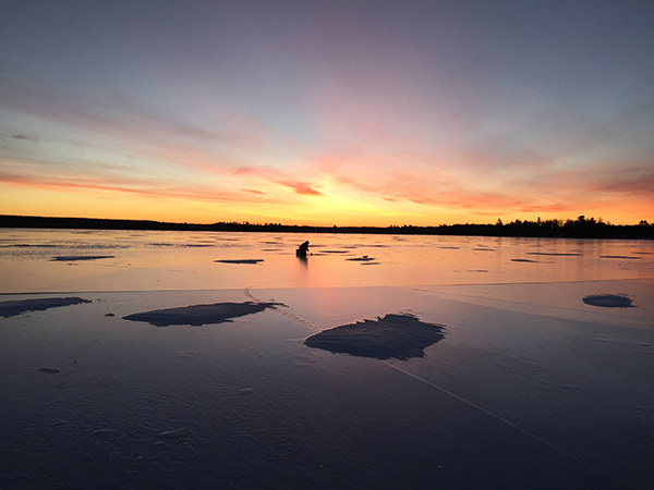 sunrise on inland lake in Michigan with ice fisherman in background
