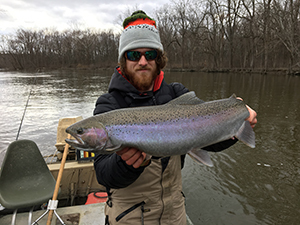 Man dressed in winter clothes on a boat, holding a steelhead