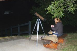 lady sitting on bench by telescope at night