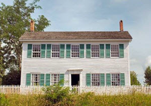Walker Tavern, viewed from the front, has white clapboard siding and green shutters on its four lower and five upper windows. 